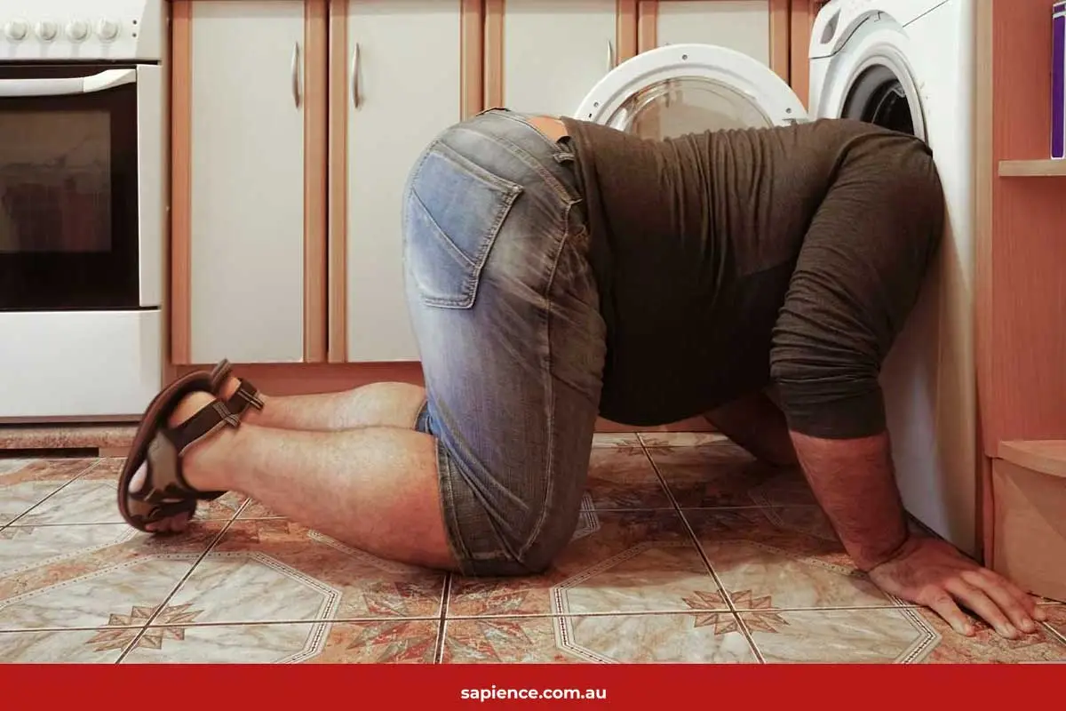 man kneeling on ground with his head in a front loader washing machine door