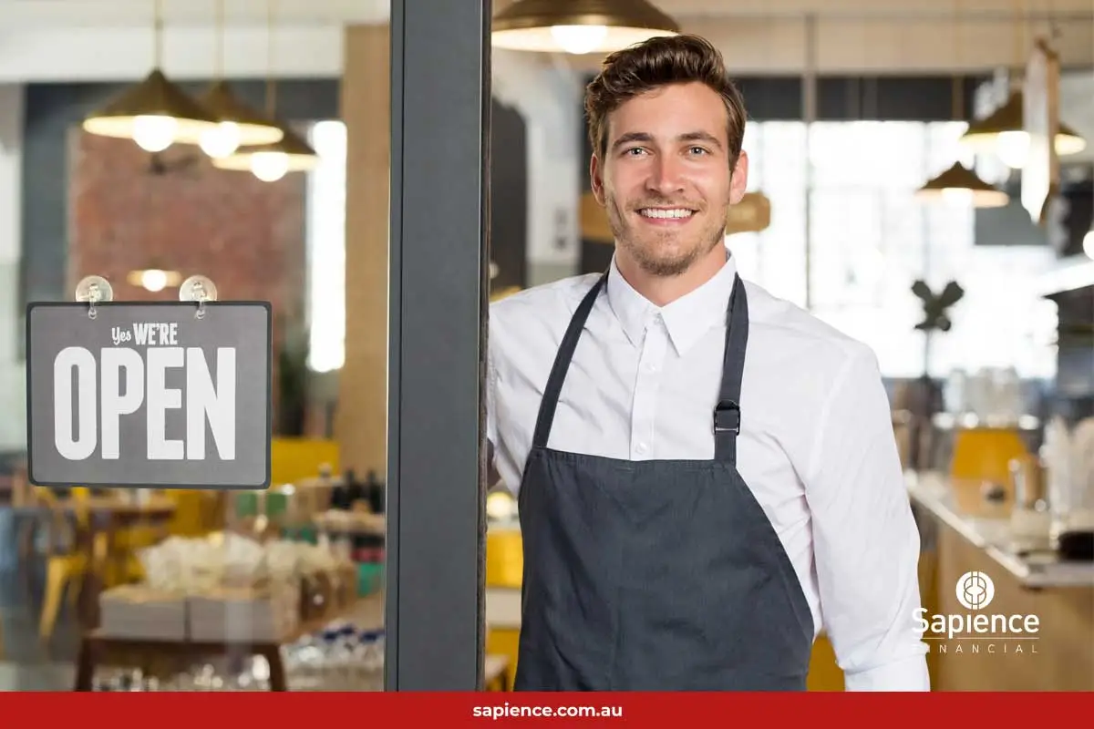 smiling proud business owner standing near an open door with the sign, Open for business